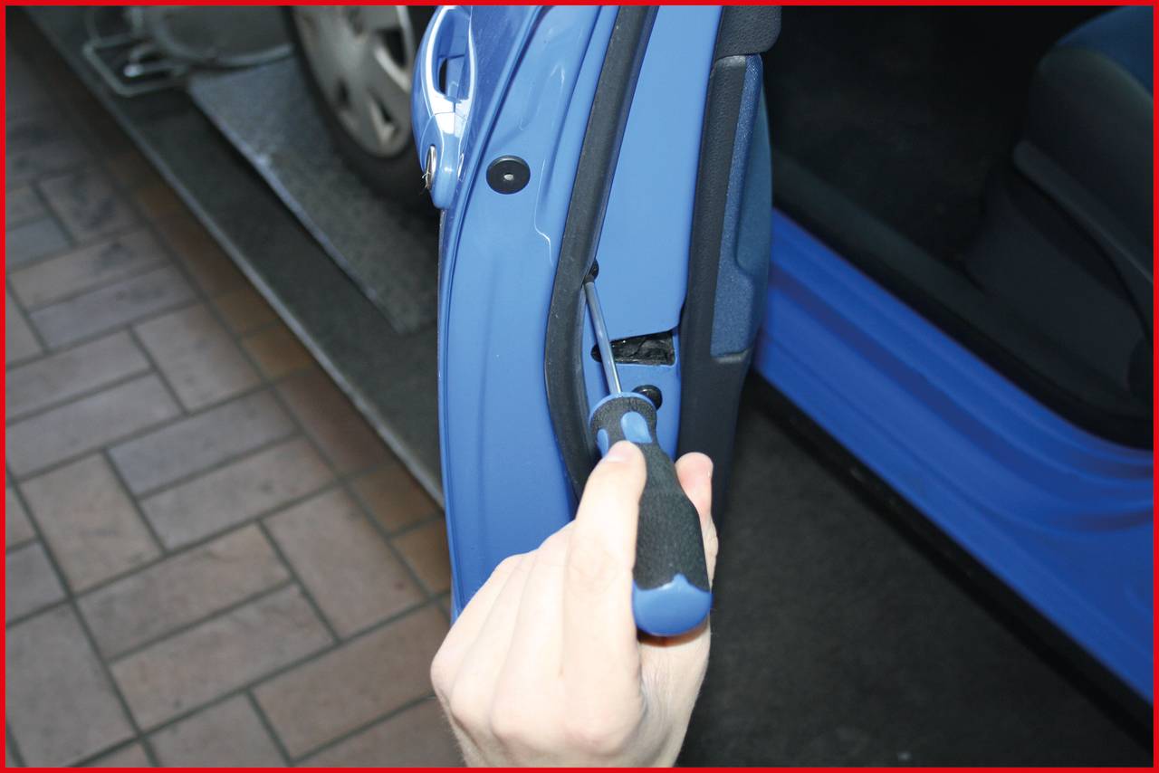 Hand hält einen Schraubenzieher und arbeitet an einer Autotürverkleidung. Die Tür ist blau und teilweise geöffnet, ein Auto im Hintergrund.