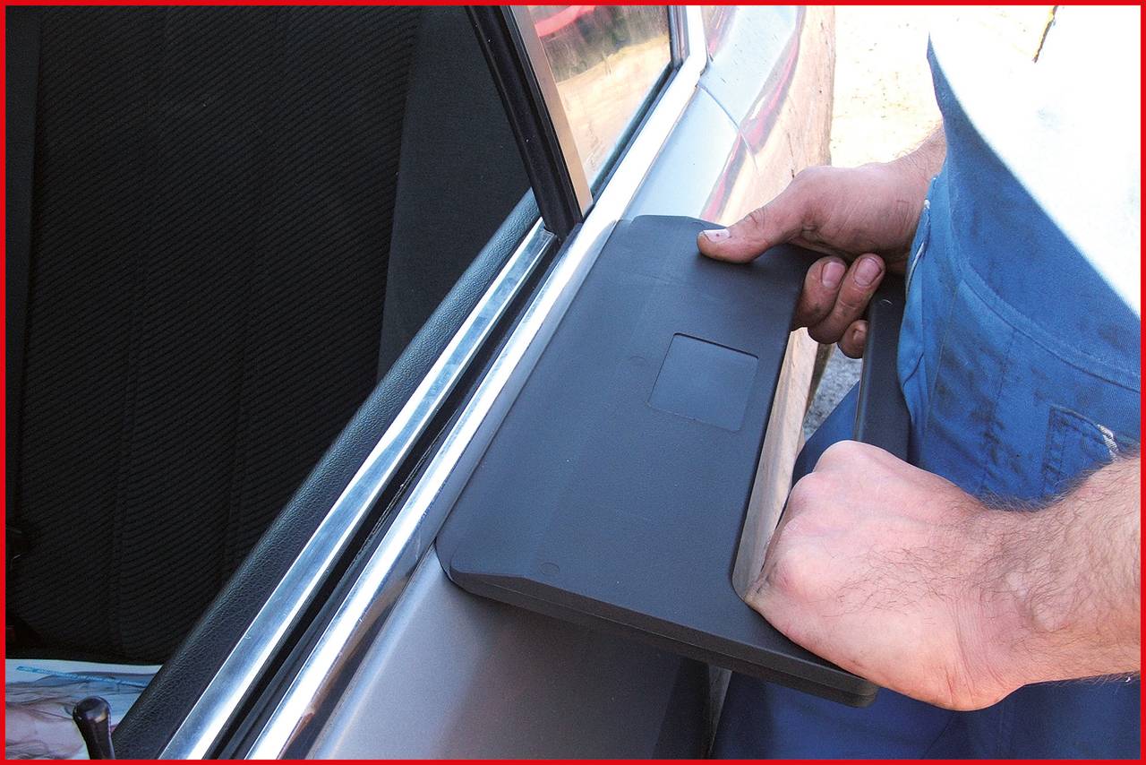 Eine Person mit blauer Kleidung verwendet ein Werkzeug zum Entriegeln einer Autotür. Hände halten das Werkzeug am Türrahmen eines silbernen Autos.
