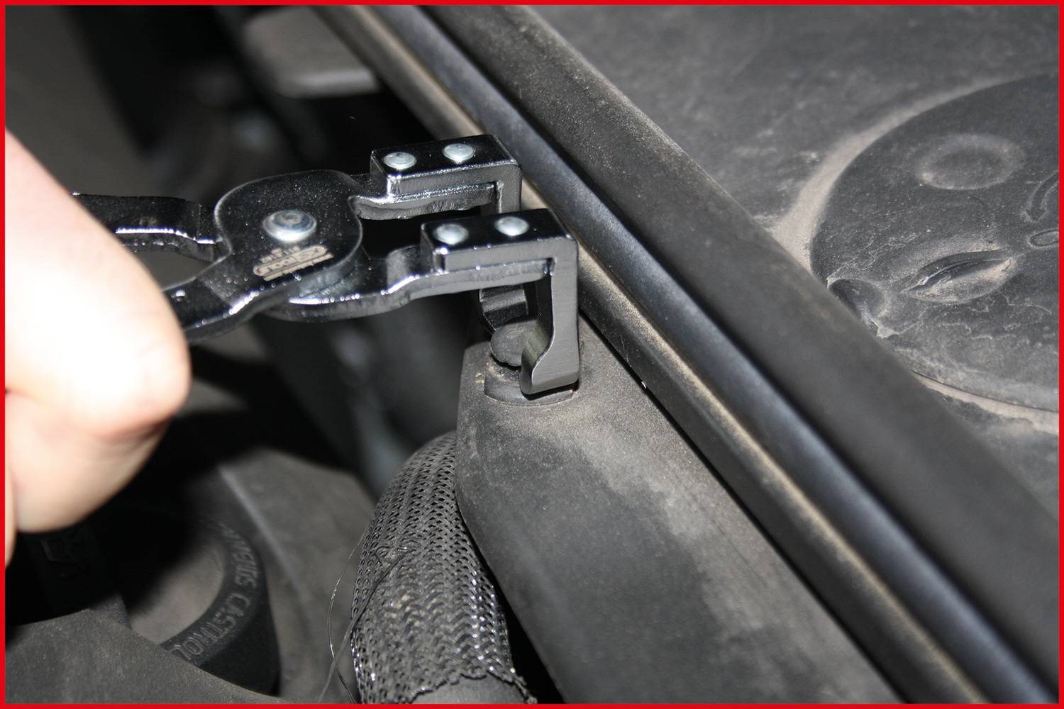 Eine Zange wird benutzt, um einen Metallclip zu lösen, der ein Kabel oder Schlauch im Motorraum eines Autos sichert.