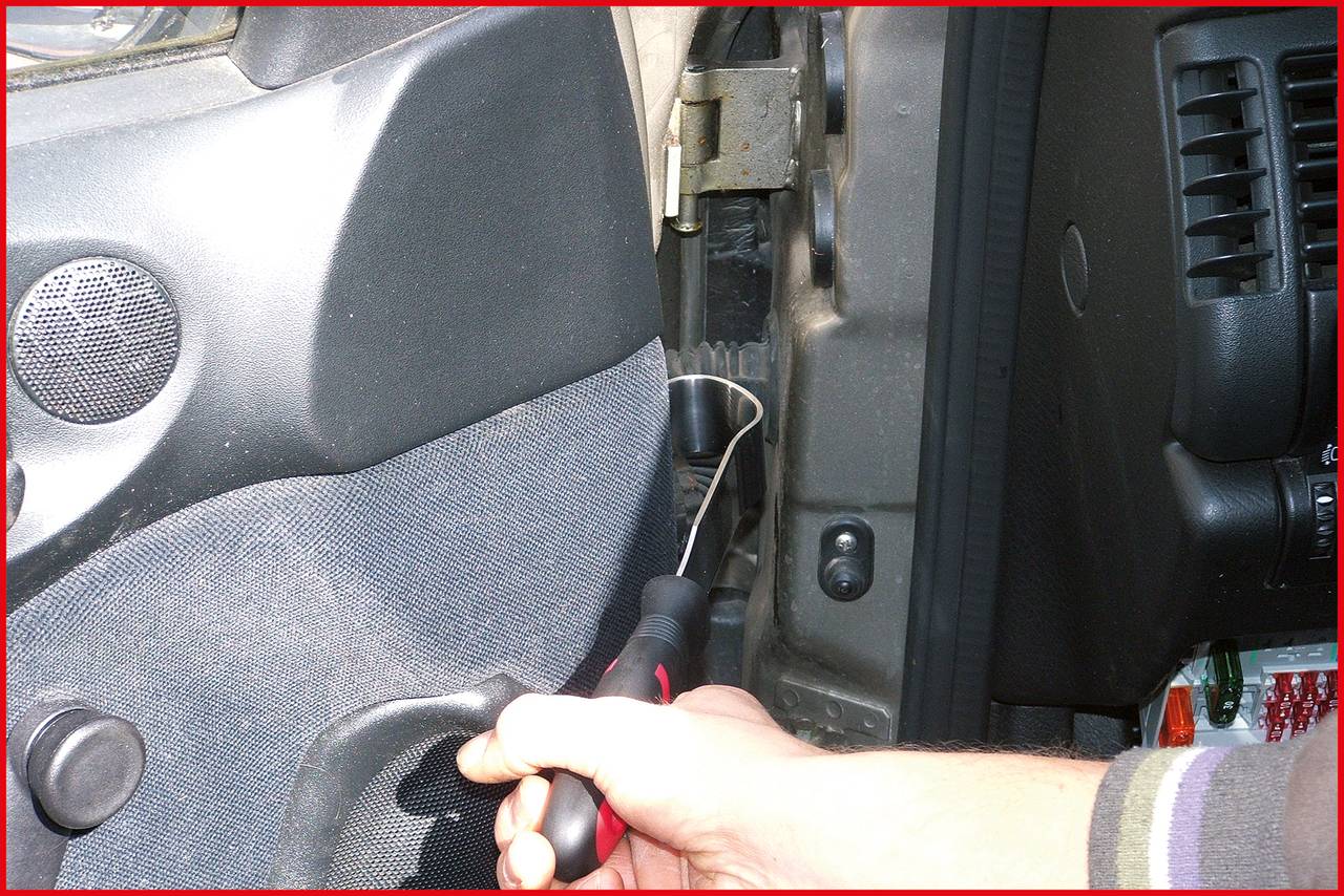 'Eine Hand hält einen Schraubenzieher, der an einer Autoscheibe angesetzt wird. Möglicher Autodiebstahl oder Reparaturversuch.'