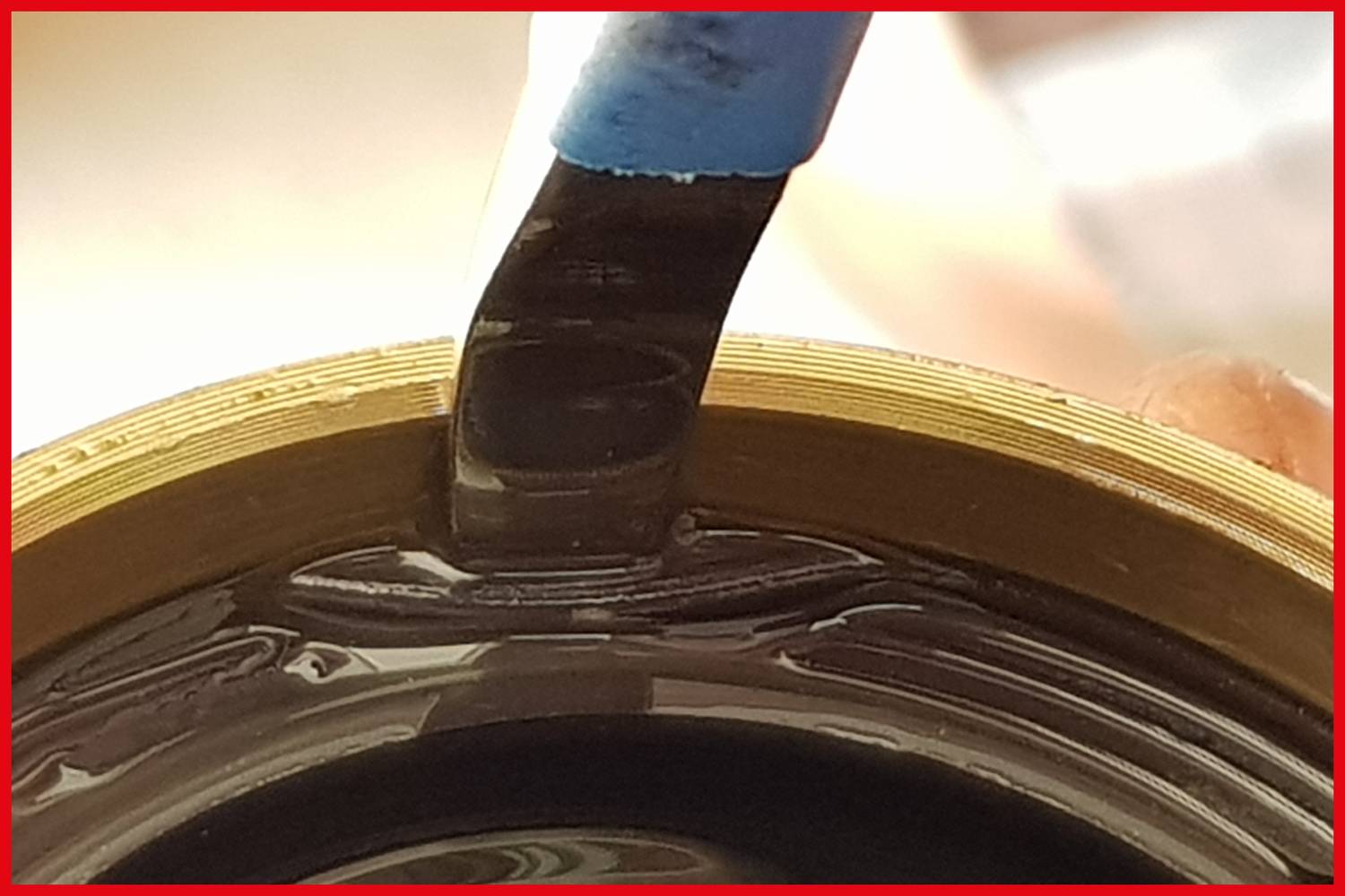 Pinsel trägt eine dunkle Flüssigkeit auf einen runden, goldfarbenen Gegenstand auf. Nahaufnahme zeigt Detailarbeit mit Präzision.