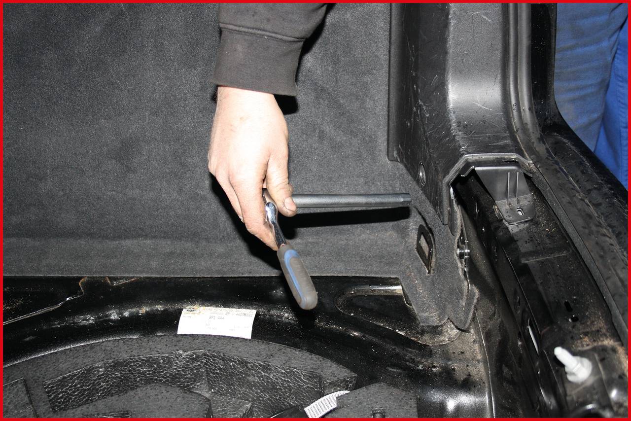 Eine Person zieht an einem Hebel im Auto, um die Rückbank nach hinten zu klappen. Die Szene zeigt den Kofferraum von innen.