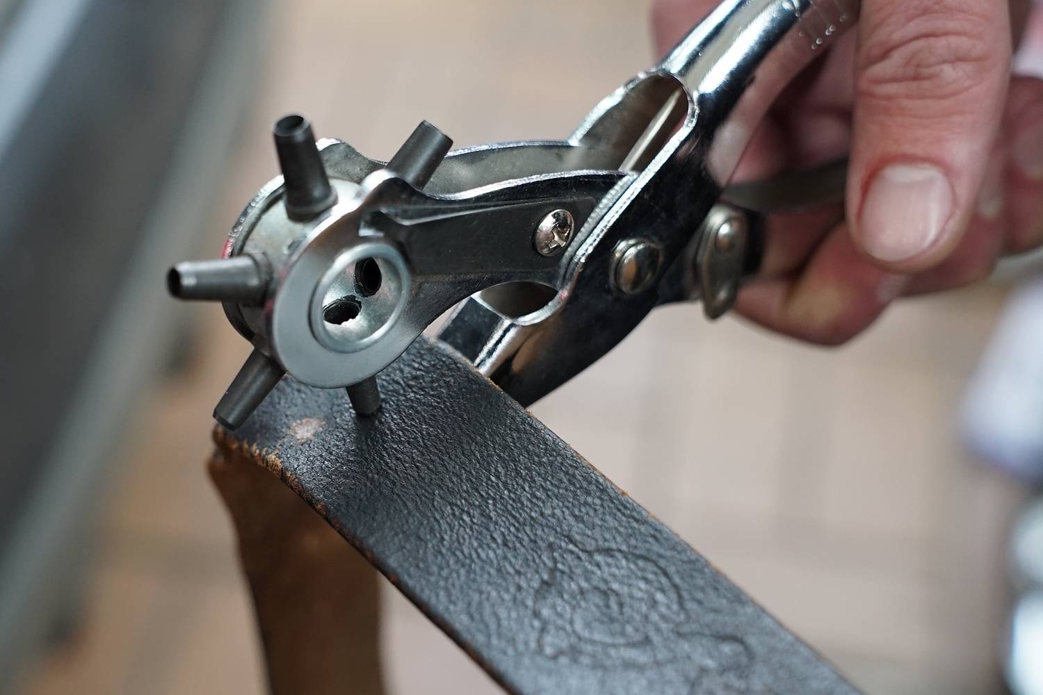 Eine Hand benutzt eine Revolverlochzange, um ein Loch in einen Ledergürtel zu stanzen. Die Zange hat mehrere Lochgrößen.