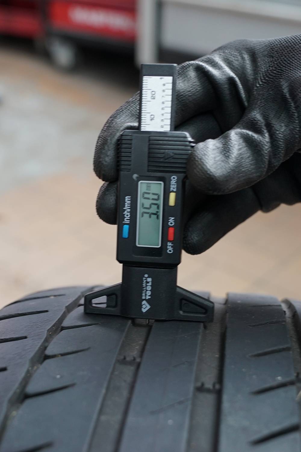 Eine behandschuhte Hand misst mit einem digitalen Messschieber die Profiltiefe eines Autoreifens. Der Messwert zeigt 3,5 mm an.