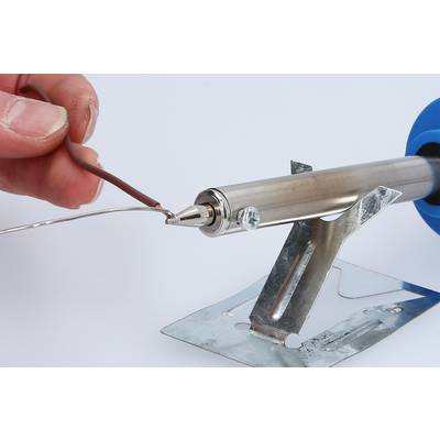 Eine Hand hält ein braunes Kabel an einem heißen Lötkolben, der auf einem metallischen Ständer ruht.