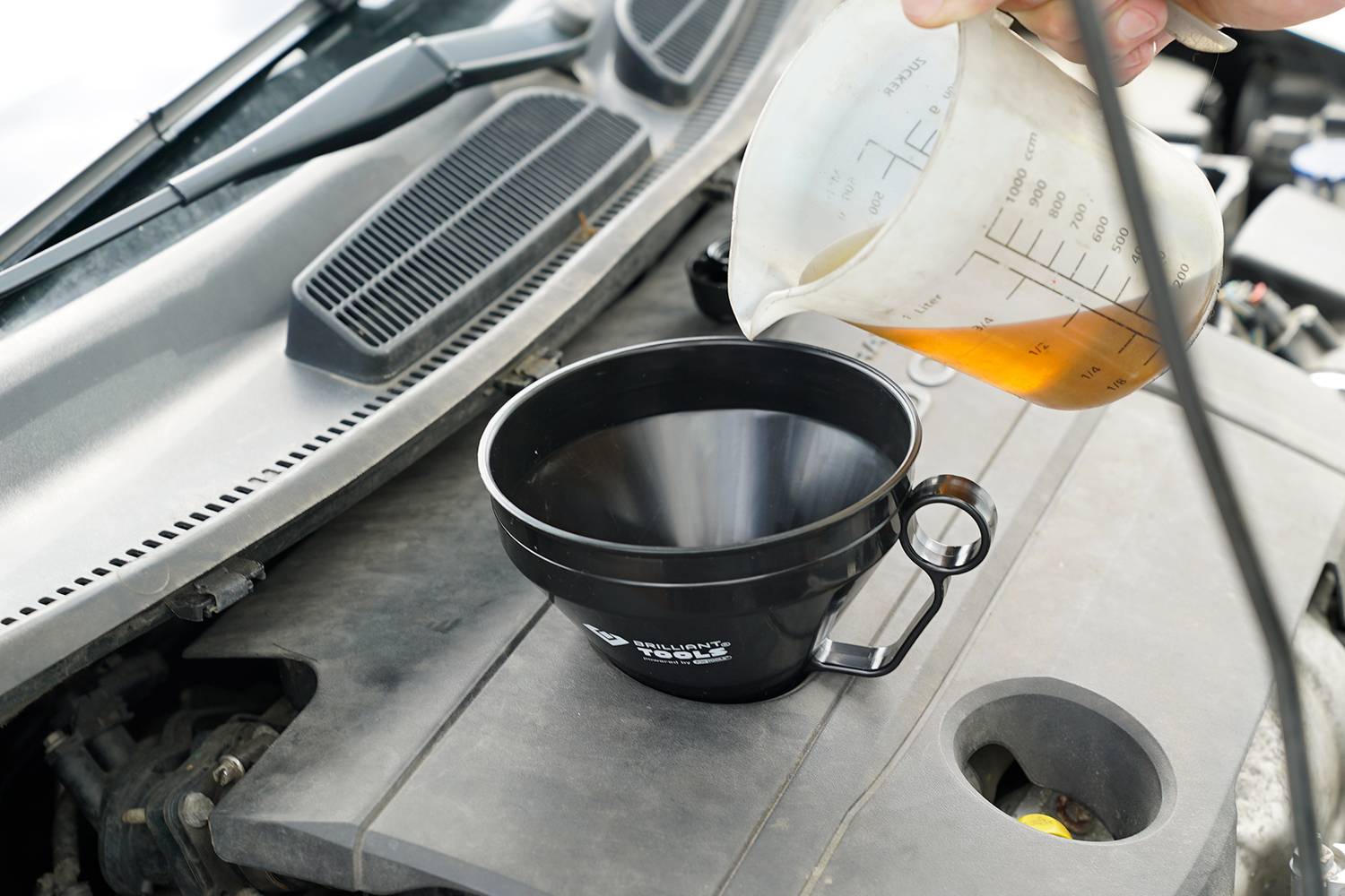 Eine Person füllt Motoröl mit einem Messbecher durch einen Trichter in den Motor eines Autos.