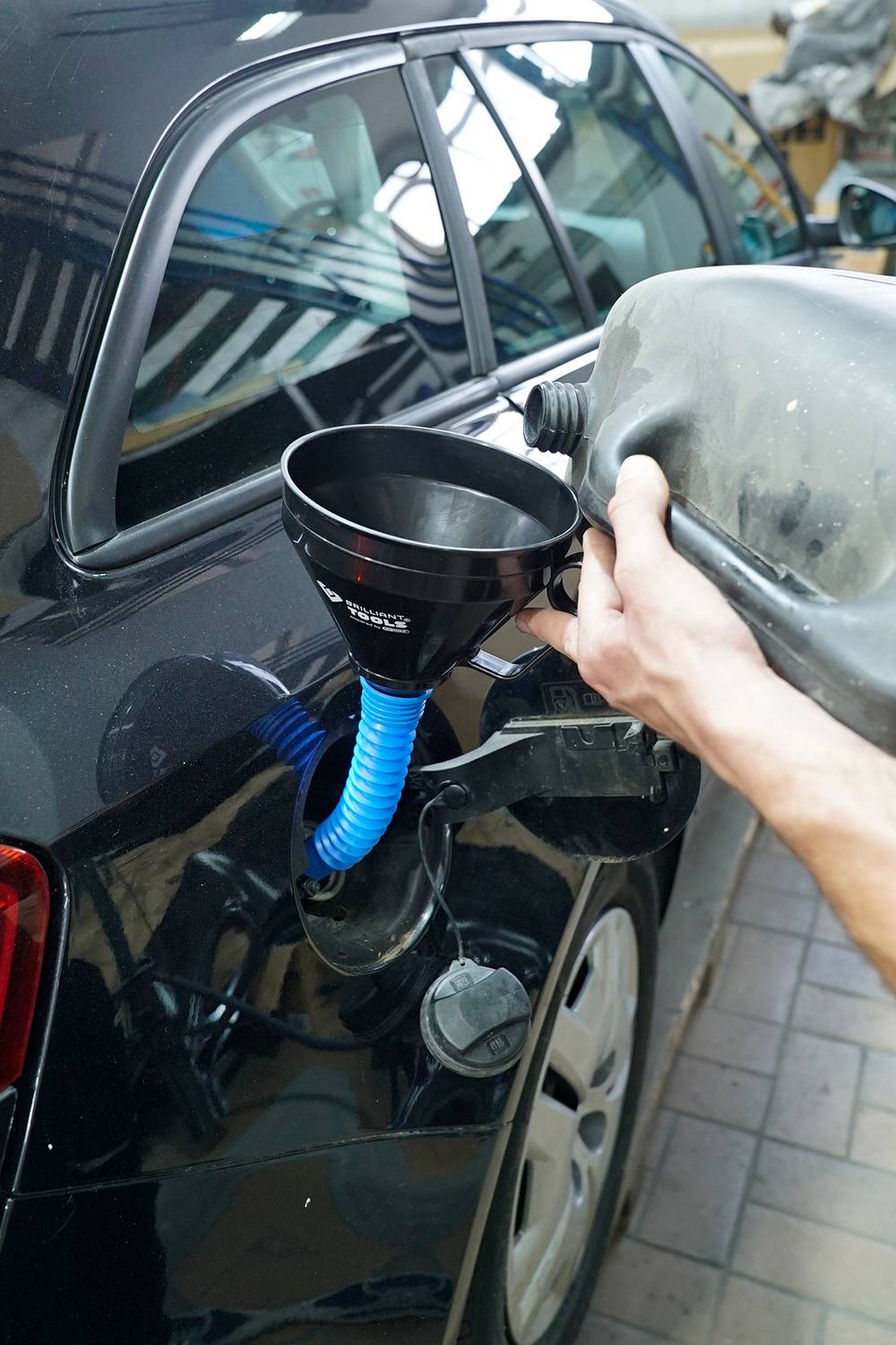 Eine Person füllt Diesel mit einem Kanister in den Tank eines schwarzen Autos. Ein blauer Trichter wird verwendet, um das Einfüllen zu erleichtern.