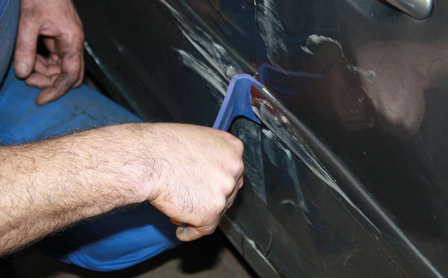 Eine Person repariert eine Autotür, indem sie Spachtelmasse aufträgt und glättet. Die Tür hat Kratzer und wird ausgebessert.