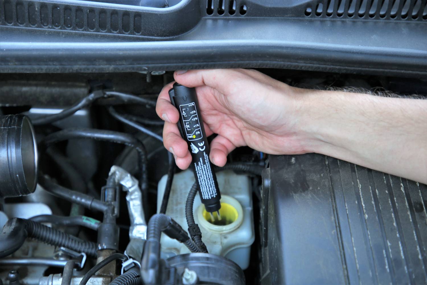 Eine Hand hält ein Testgerät über den Bremsflüssigkeitsbehälter in einem Auto, um die Bremsflüssigkeit zu überprüfen.