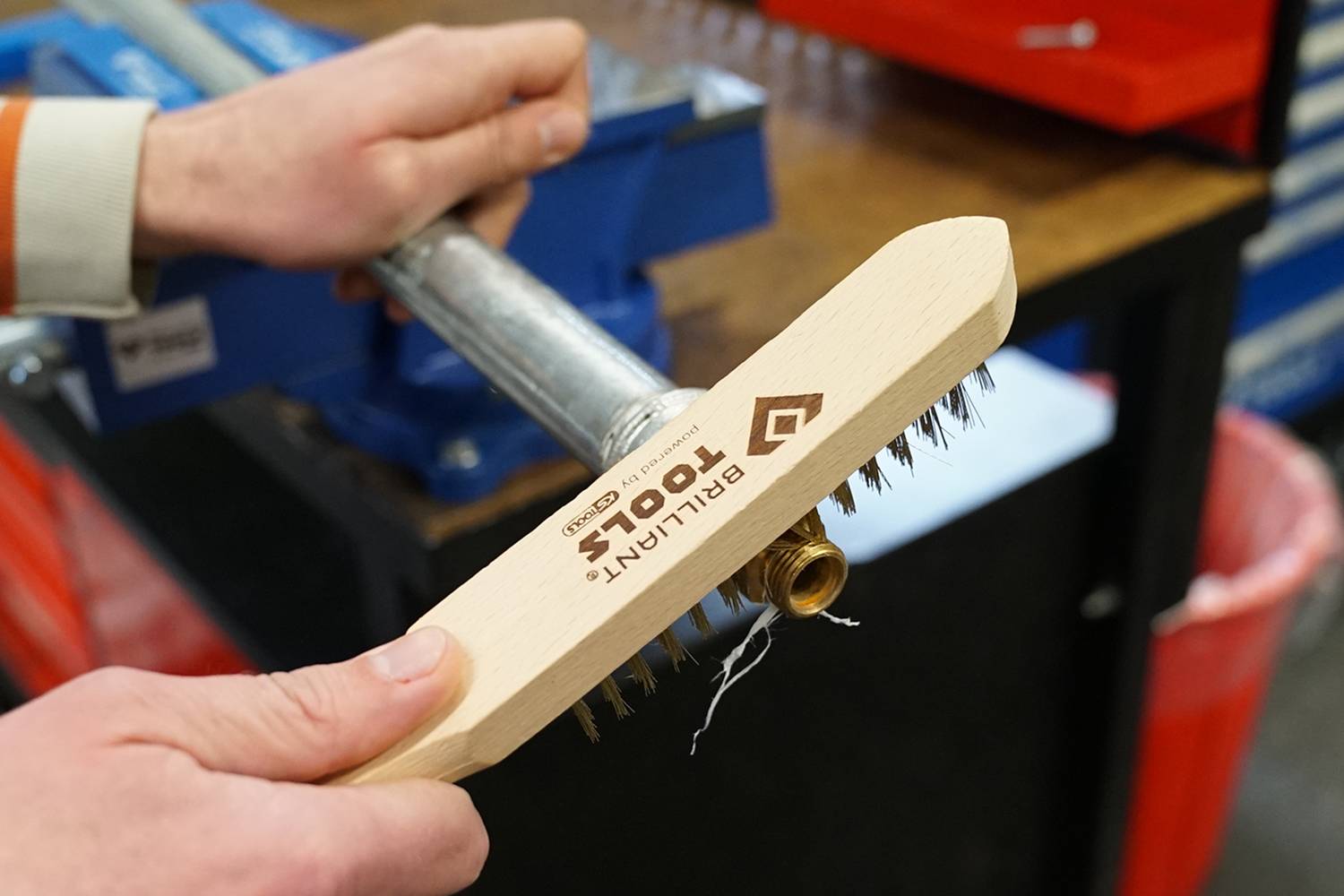 Eine Person reinigt ein Metallrohr mit einer Drahtbürste an einem Arbeitsplatz.