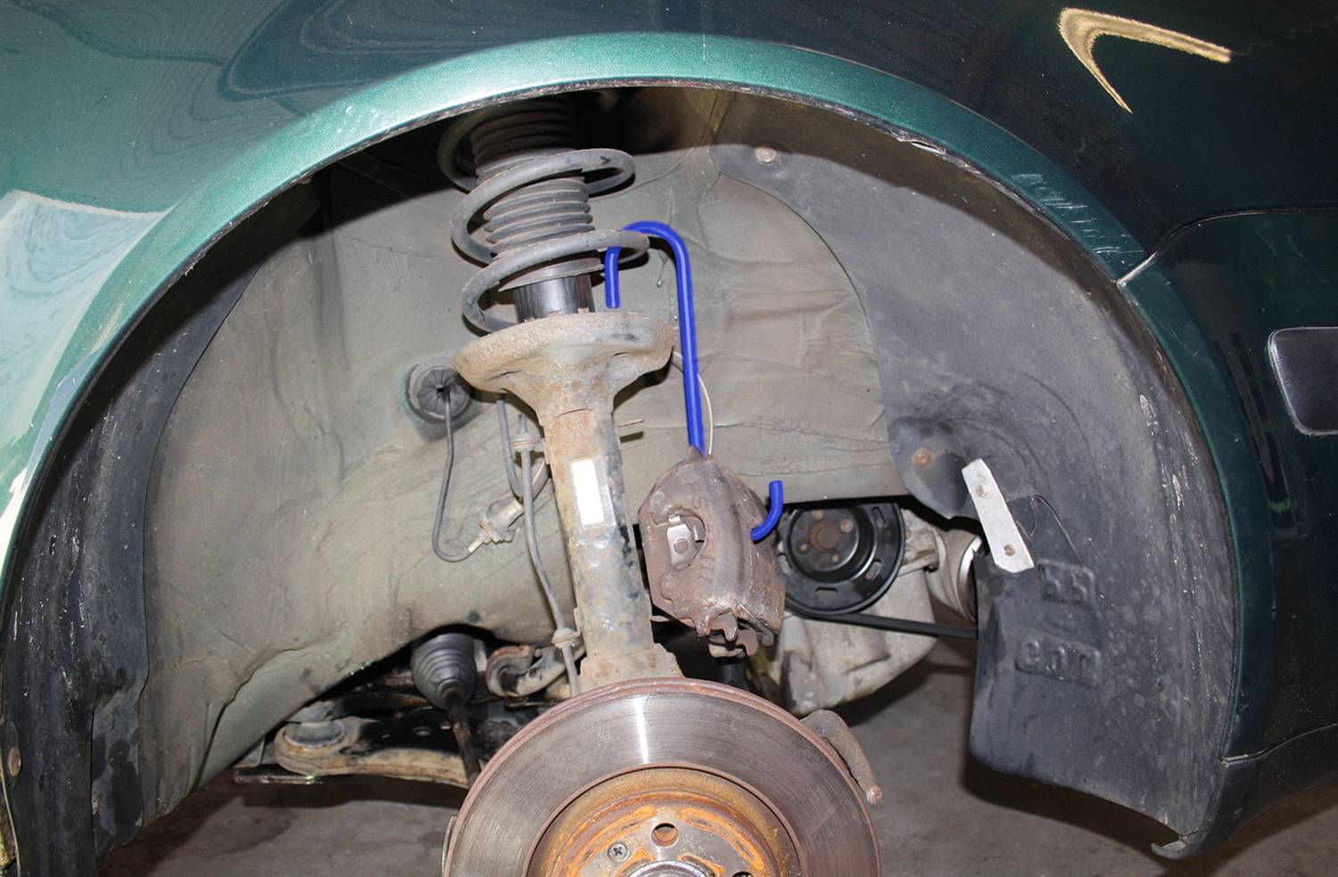 Fahrzeugradkasten mit sichtbarer Federung und Bremsanlage eines Autos. Enthält Stoßdämpfer, Bremsscheibe und Bremssattel.