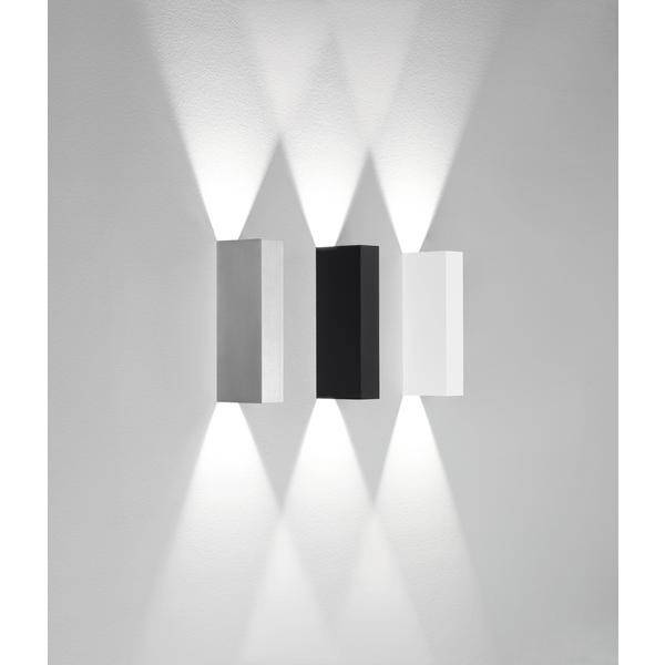 Drei rechteckige Wandleuchten in Grau, Schwarz und Weiß leuchten jeweils nach oben und unten und erzeugen symmetrische Lichtmuster an der Wand.