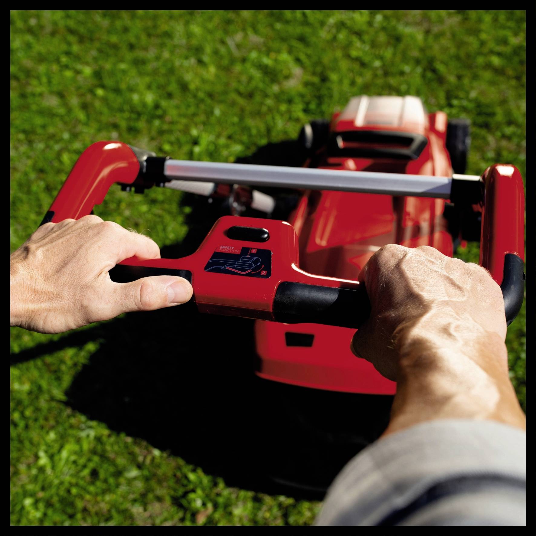 Person bedient einen roten Rasenmäher auf einer grünen Wiese, er greift die Griffe fest.