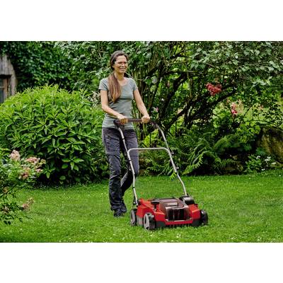 Eine Frau mäht Rasen mit einem roten Rasenmäher in einem Garten, umgeben von grünen Pflanzen und Bäumen.