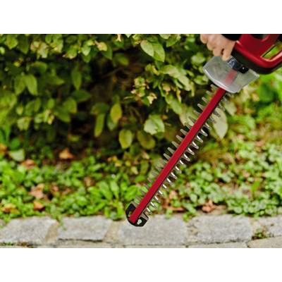 Eine Person hält eine rote Heckenschere vor einem grünen Busch. Die Schere ist betriebsbereit und wird zum Schneiden von Zweigen verwendet.