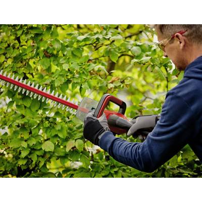 Mann schneidet Büsche mit elektrischer Heckenschere, trägt Schutzbrille und Handschuhe.