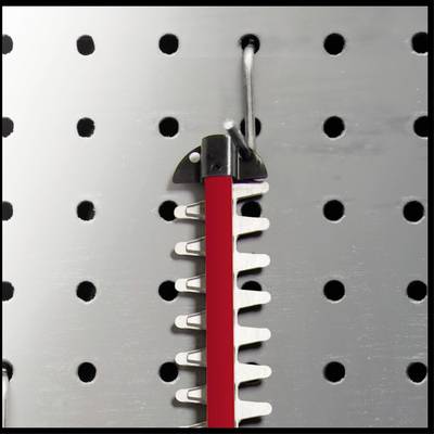 Ein rotes Werkzeug hängt an einem Haken auf einer Lochwand. Es hat gezackte Metallkanten, die für Schneidearbeiten geeignet sind.