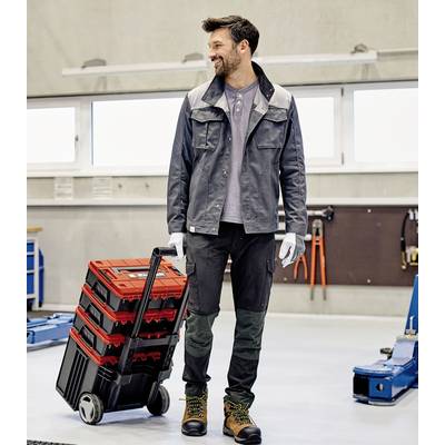Ein Mann in Arbeitskleidung steht in einer Werkstatt und zieht einen Trolley mit roten Werkzeugkoffern.