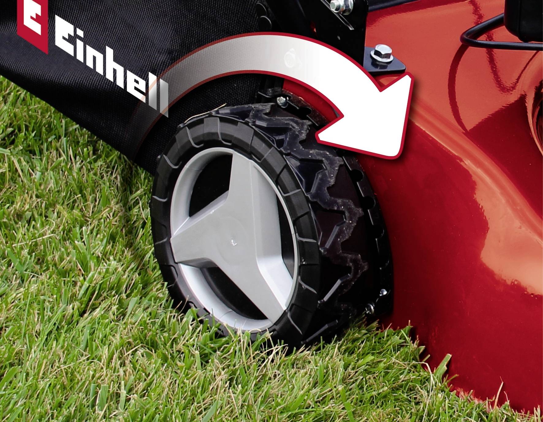 Ein roter Rasenmäher auf Rasen, Fokus auf dem Reifen mit einem weißen Pfeil, der auf den Drehpunkt zeigt. Rechts ist der Markenname sichtbar.