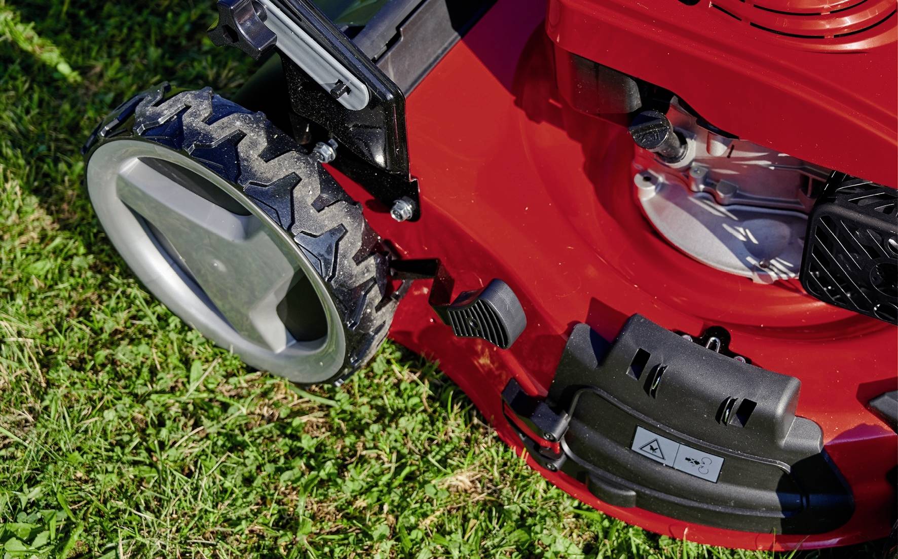 Ein roter Rasenmäher steht auf grünem Gras. Große, profilierte Räder und ein Motorgehäuse sind sichtbar.
