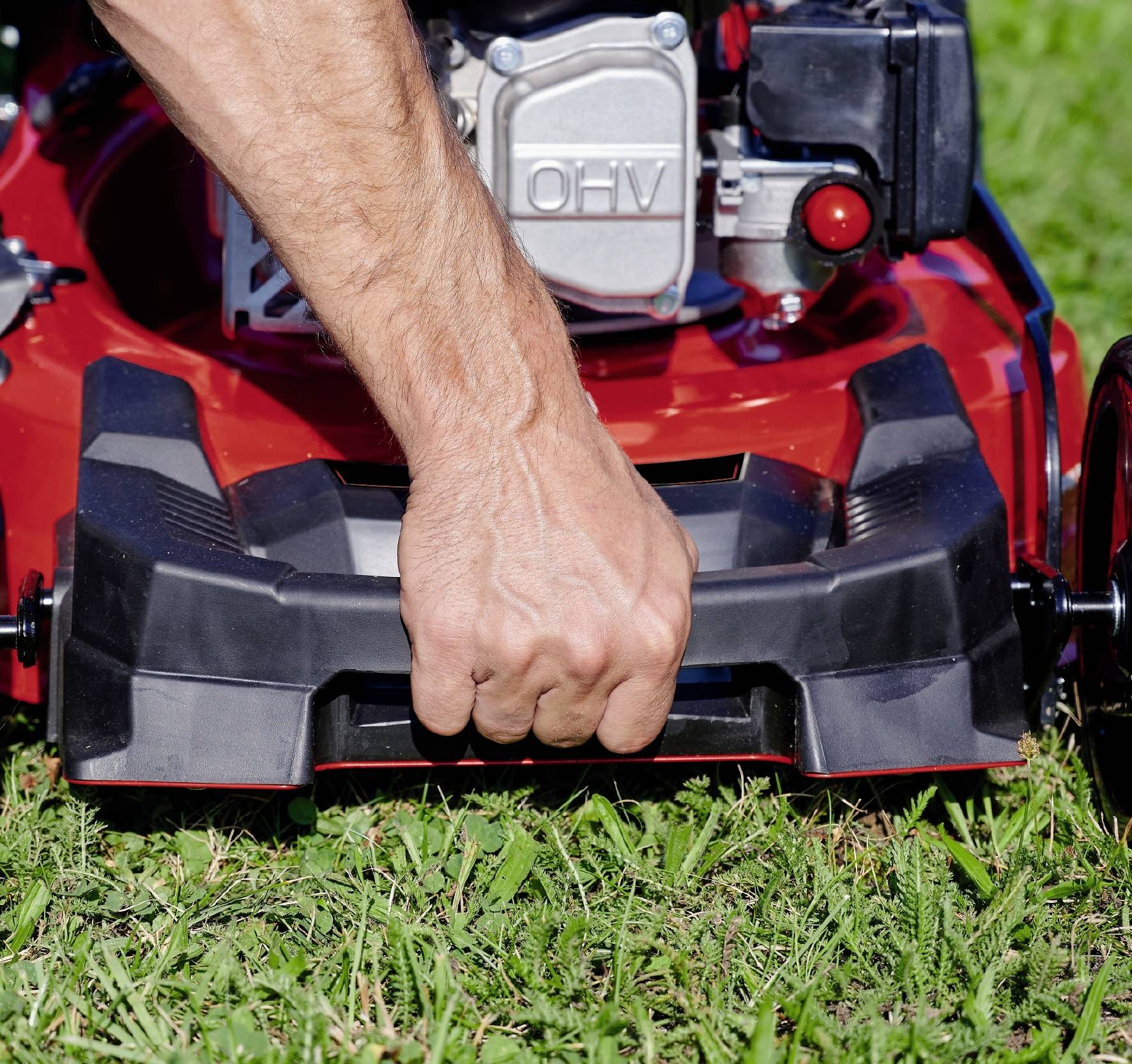 Eine Person hält den Griff eines Rasenmähers auf grünem Gras, bereit, ihn zu starten oder zu bewegen.