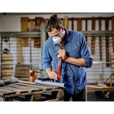 Ein Mann in Schutzbrille und Mundschutz bearbeitet ein Metallrohr mit einer Elektrosäge in einer Werkstatt.