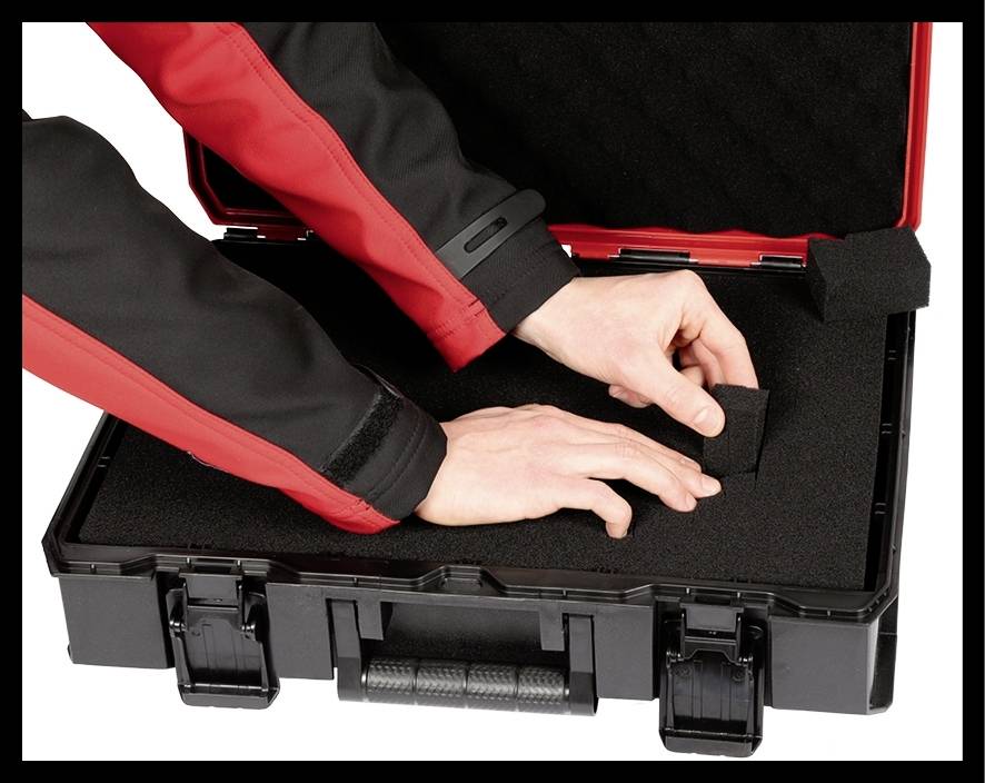 Eine Person entfernt Schaumstoffstücke aus einem schwarzen Koffer, möglicherweise zum Anpassen des Innenraums für den Transport empfindlicher Gegenstände.