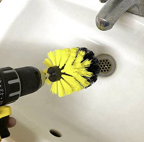 Akkubohrer mit Bürstenaufsatz reinigt ein Waschbecken. Gelb-schwarze Bürste dreht sich, um Verunreinigungen zu entfernen.