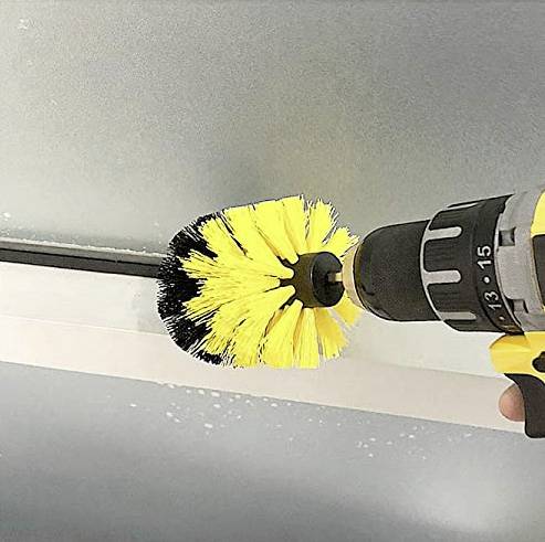 Eine elektrische Bohrmaschine mit gelber Bürstenaufsatz wird verwendet, um eine Oberfläche zu reinigen.