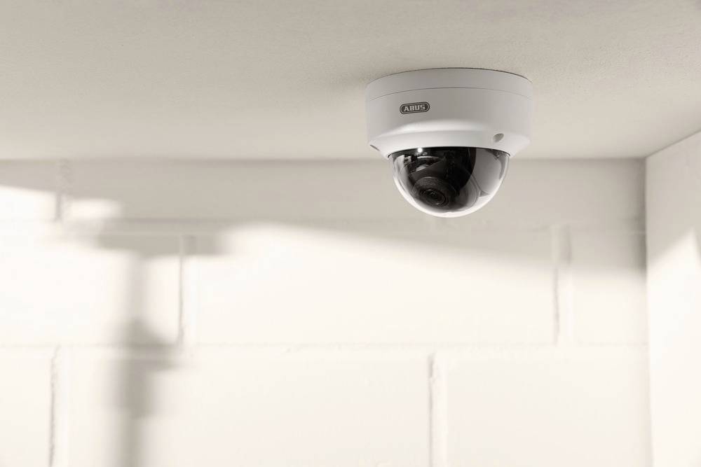 Überwachungskamera an der Decke eines hellen Raumes, zeigt auf eine Ecke mit weißen Ziegelwänden.