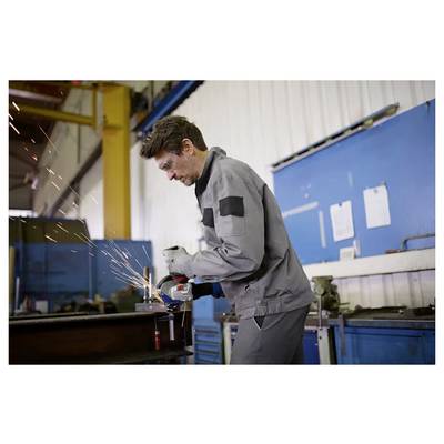 Eine Person in Schutzausrüstung verwendet einen Schleifer und erzeugt Funken in einer Industriewerkstatt mit blauen und weißen Wänden im Hintergrund.