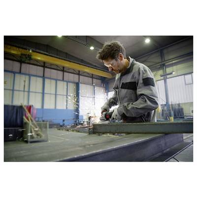 Eine Person in einer Werkstatt, die einen Schleifer auf einem Metallträger einsetzt, wobei Funken in einer großen Industrieanlage fliegen.