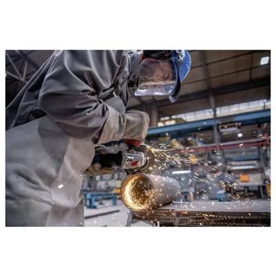 Ein Arbeiter mit Schutzausrüstung verwendet einen Winkelschleifer, um ein Metallrohr zu schneiden, wobei in einer industriellen Werkstattumgebung Funken entstehen.