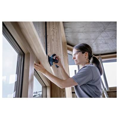 Eine Person, die einen Elektro-Schleifer verwendet, um einen Holzfensterrahmen zu glätten. Sie trägt Schutzbrille und Gehörschutz in einem gut beleuchteten Raum.