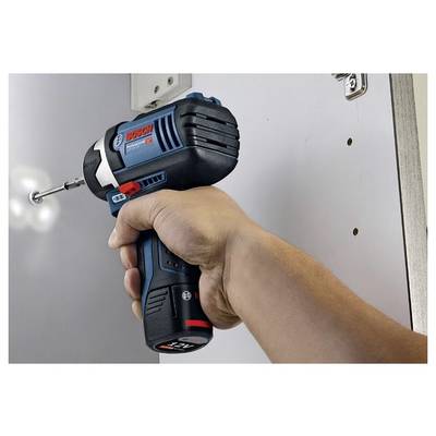 Eine Person verwendet eine blaue und schwarze kabellose Bohrmaschine, um in eine weiße Oberfläche zu schrauben. Die Bohrmaschine hat einen roten Knopf und eine Markenbeschriftung darauf.