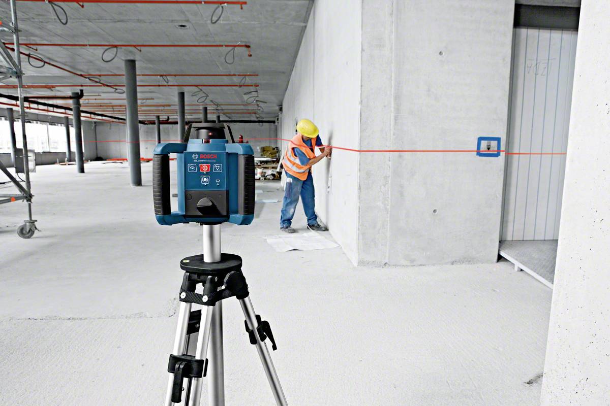 Ein Bauarbeiter nutzt ein Laser-Messgerät auf einem Stativ, um präzise Markierungen auf einer Betonwand auf einer Baustelle vorzunehmen.