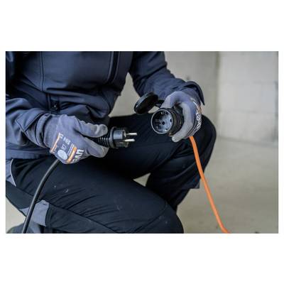 Eine Person mit Handschuhen steckt ein oranges Verlängerungskabel in einen schwarzen Stromstecker und bereitet eine elektrische Verbindung vor.