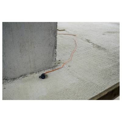 Oranges Verlängerungskabel mit schwarzem Stecker verläuft entlang eines Betonbodens neben einer großen Betonssäule.