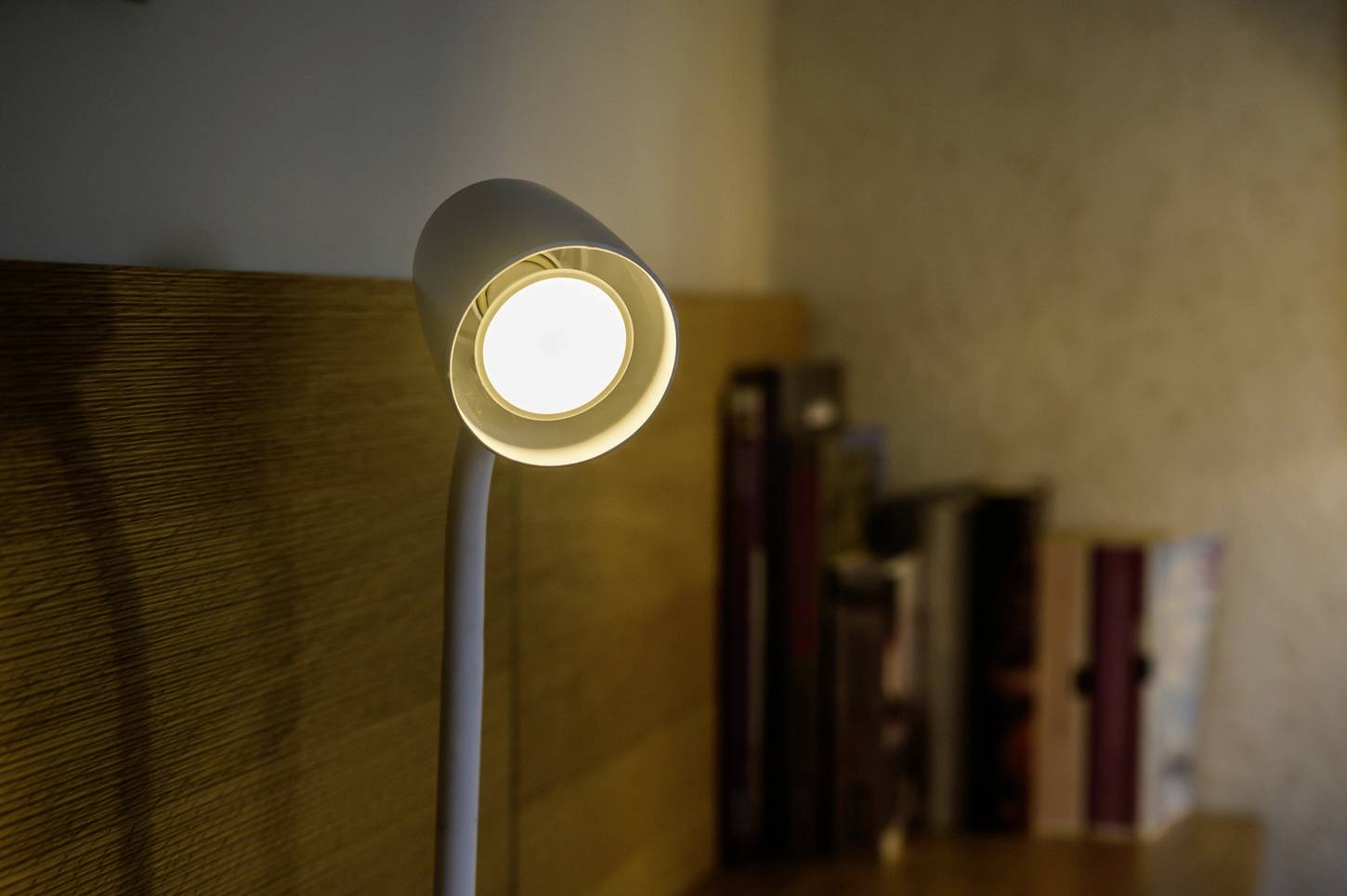 Eine eingeschaltete Leselampe wirft warmes Licht auf ein Bücherregal im Hintergrund.
