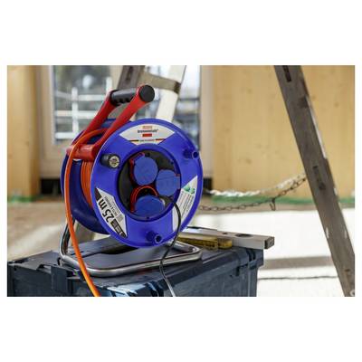 Blau-rote Kabelrolle auf einer Werkbank mit orangefarbenem Verlängerungskabel und Steckdosen in einer Werkstatt- oder Baustelle.
