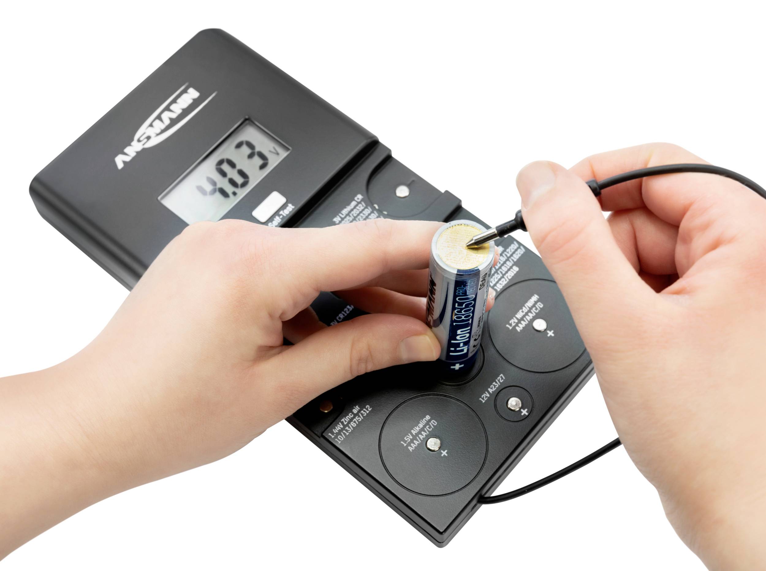 Person testet eine AA-Batterie mit einem Multimeter. Die Anzeige zeigt '4.03'. Das Gerät ist schwarz und hat Knöpfe zur Einstellung.