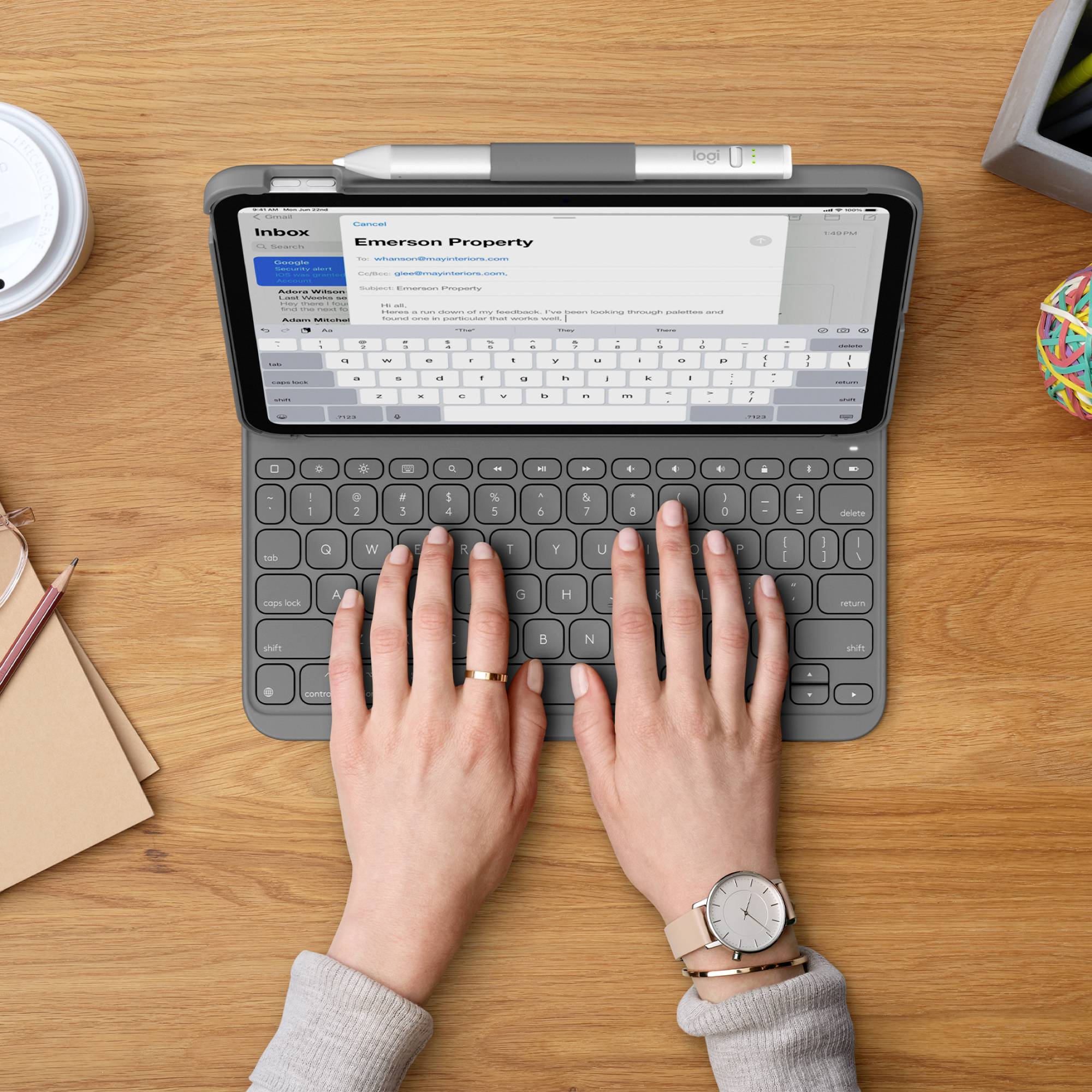 Die Person tippt auf einem Tablet mit Tastatur auf einem Holztisch. Der Bildschirm zeigt eine E-Mail mit dem Betreff 'Emerson Property'.