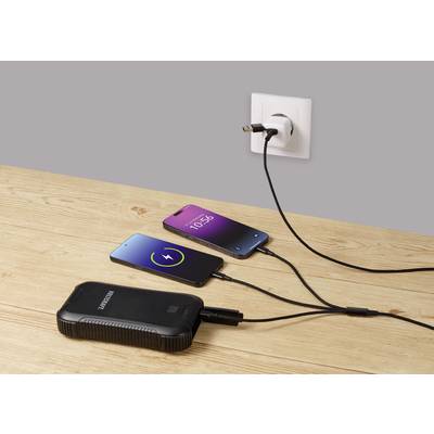 Zwei Smartphones liegen auf einem Holztisch und laden. Eines zeigt einen grünen Ladebildschirm, das andere die Uhrzeit 10:56 an. Sie sind mit einer Steckdose und einer Powerbank verbunden.