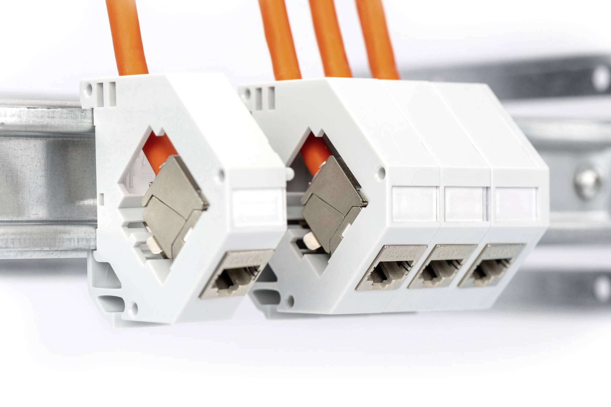 Zwei weiße, rechteckige elektrische Komponenten mit jeweils drei orangefarbenen Kabeln sind an einer Metallschiene montiert.