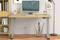 Moderner Holzschreibtisch mit Computer, Tastatur, Büromaterialien und Stehlampe in einem Bürozimmer. Behagliche Arbeitsumgebung.