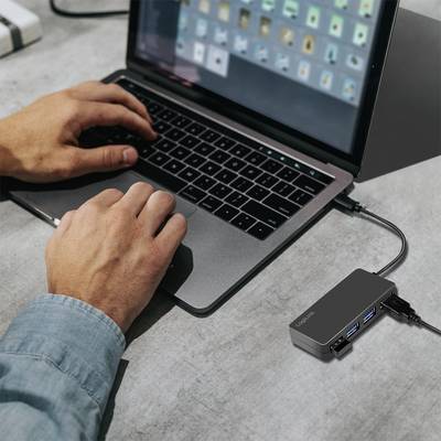 Person arbeitet an einem Laptop, der mit einem USB-Hub verbunden ist; Hände auf der Tastatur, Hub hat mehrere Anschlüsse.