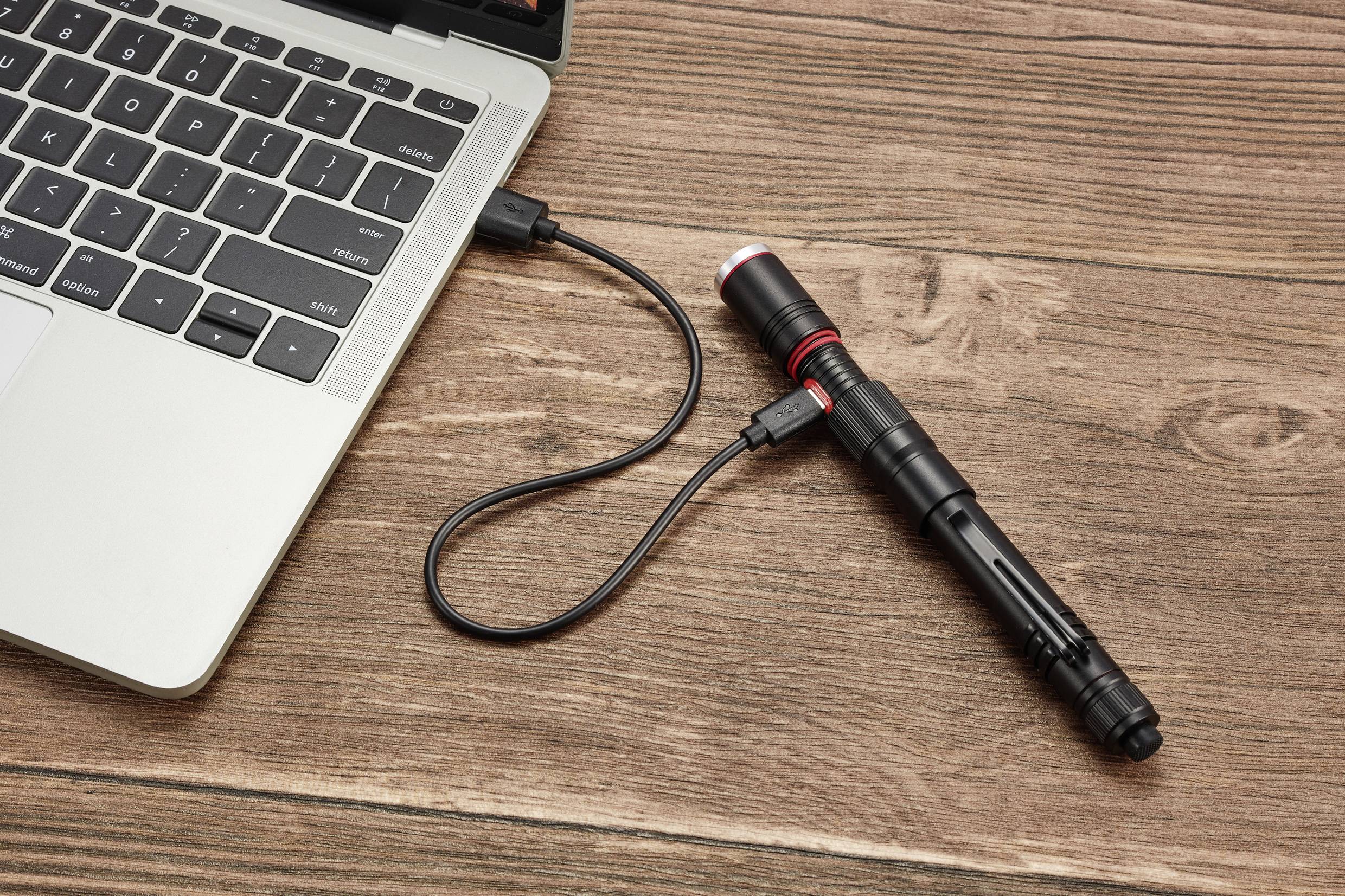 Taschenlampe über USB-Kabel mit einem Laptop verbunden, liegt auf einem Holztisch.
