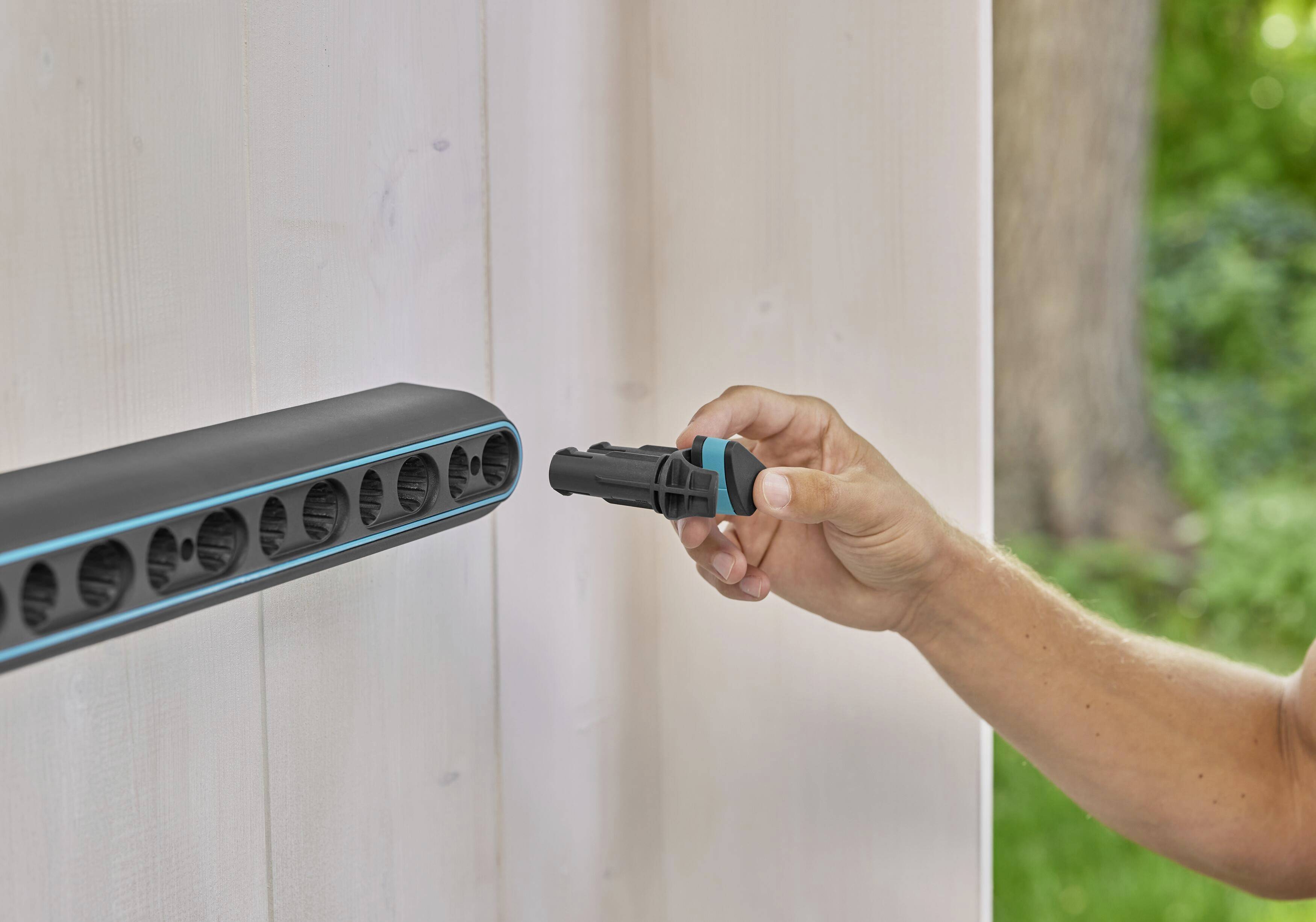 Eine Person verbindet einen schwarzen Stecker mit einer horizontalen, montierten Leiste auf einer Wand im Freien.