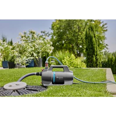 Eine Gartenpumpe auf einem Rasen, umgeben von Pflanzen, ist mit einem Schlauch verbunden und bereit zur Wasserbewässerung.