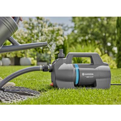 Eine Gießkanne wird mit Wasser aus einer Gardena Gartenpumpe auf einem grünen Rasen befüllt, umgeben von Bäumen und Pflanzen.